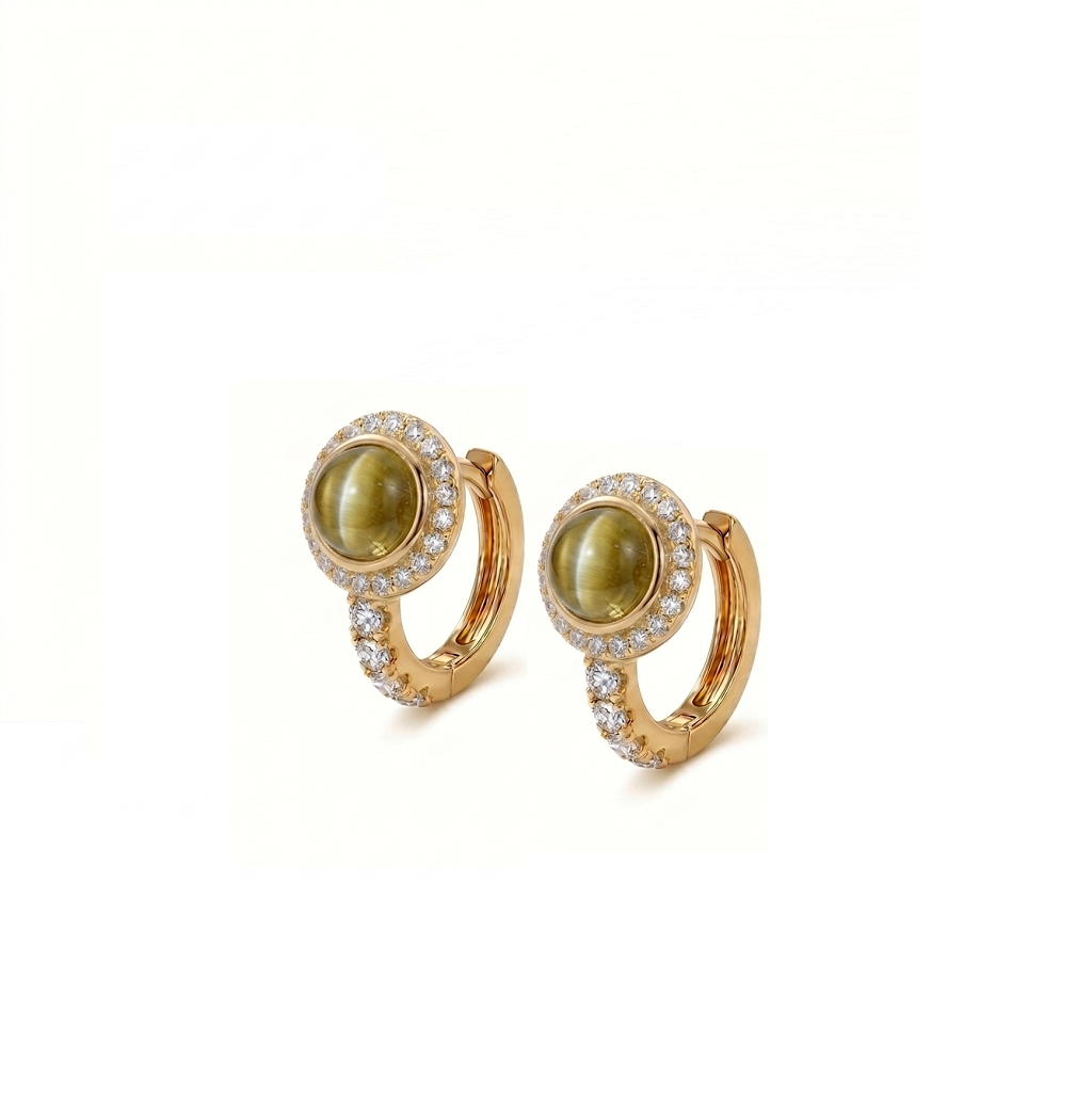 A pair of gold huggie hoop earrings featuring oval green cat's eye stones surrounded by a halo of small clear pavé stones, set against a plain white background.